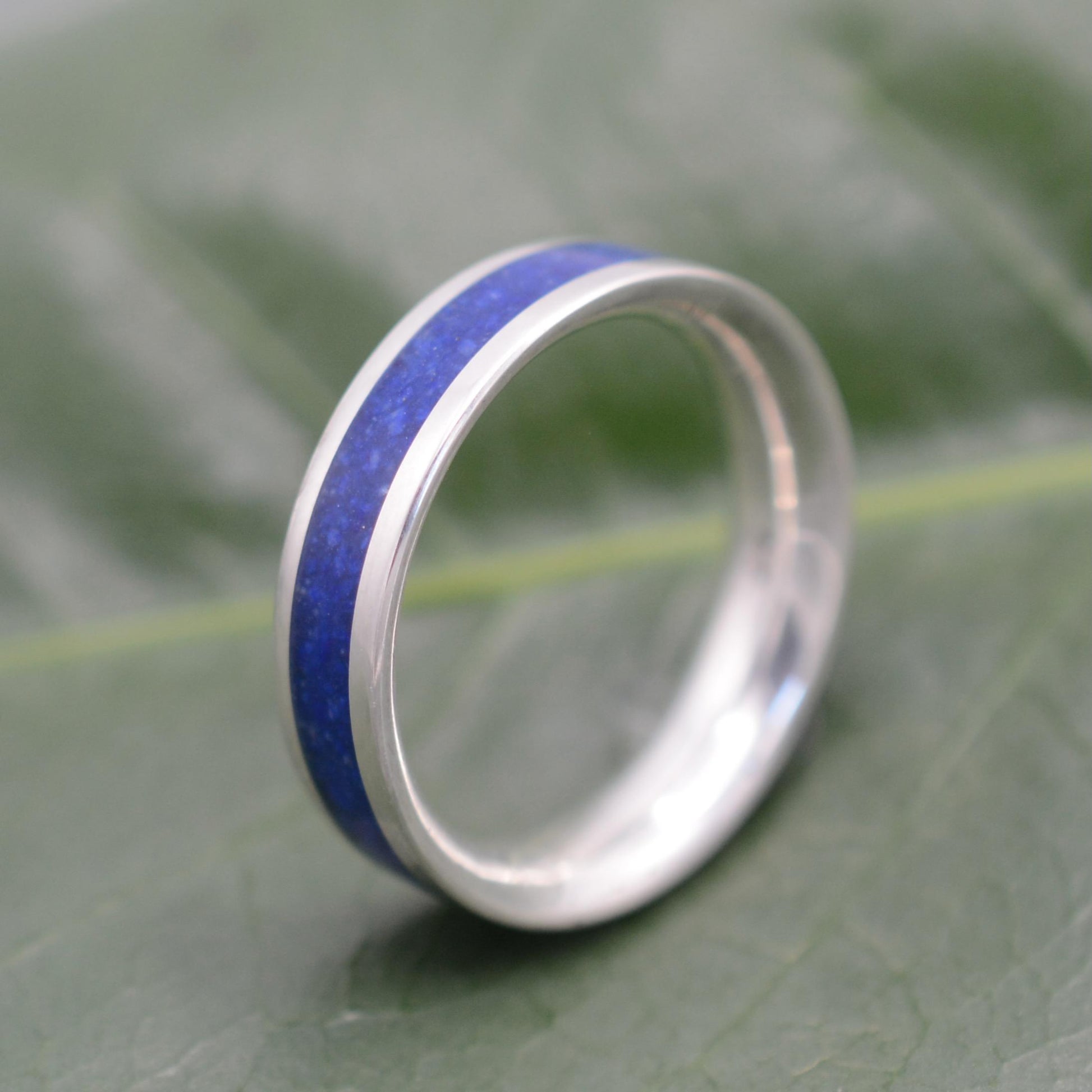 a wedding ring with a blue stripe on a green leaf