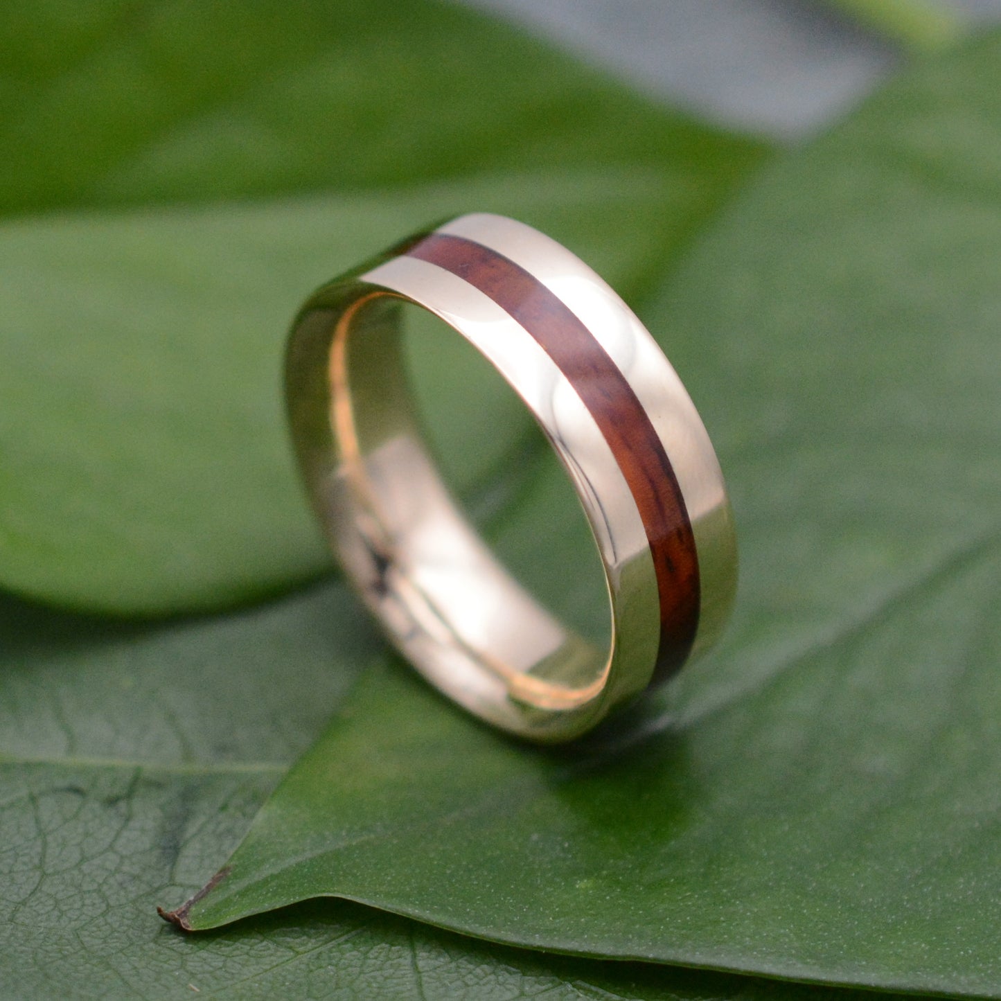a gold ring with a wooden inlay on a green leaf