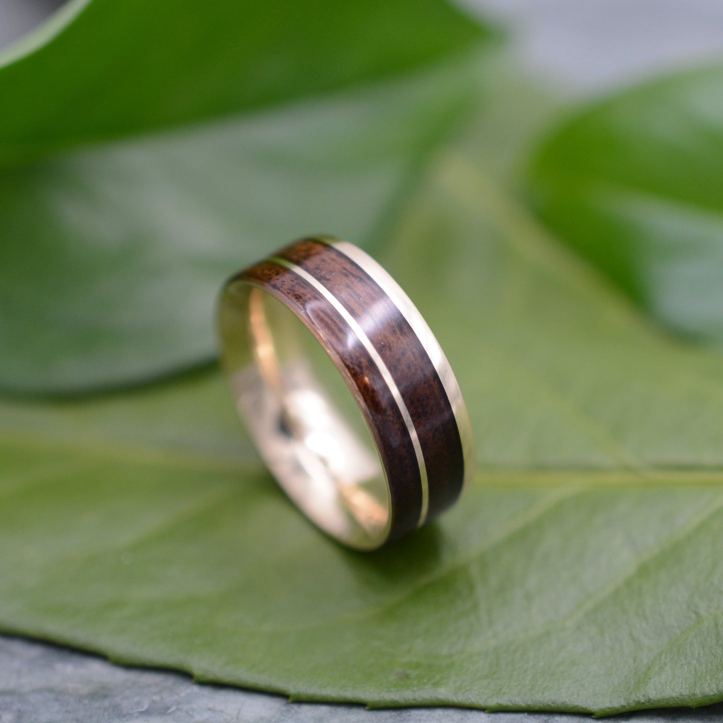 a wedding ring with a wooden inlay sits on a leaf