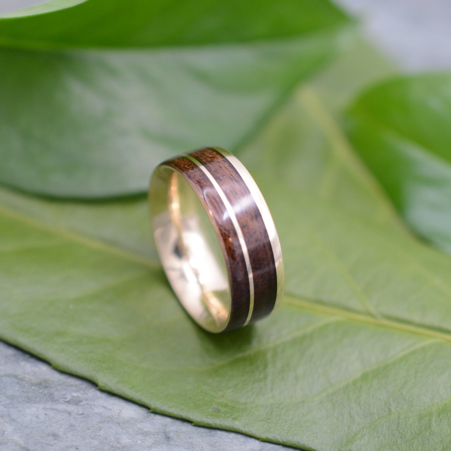 a wedding ring with a wooden inlay sits on a leaf