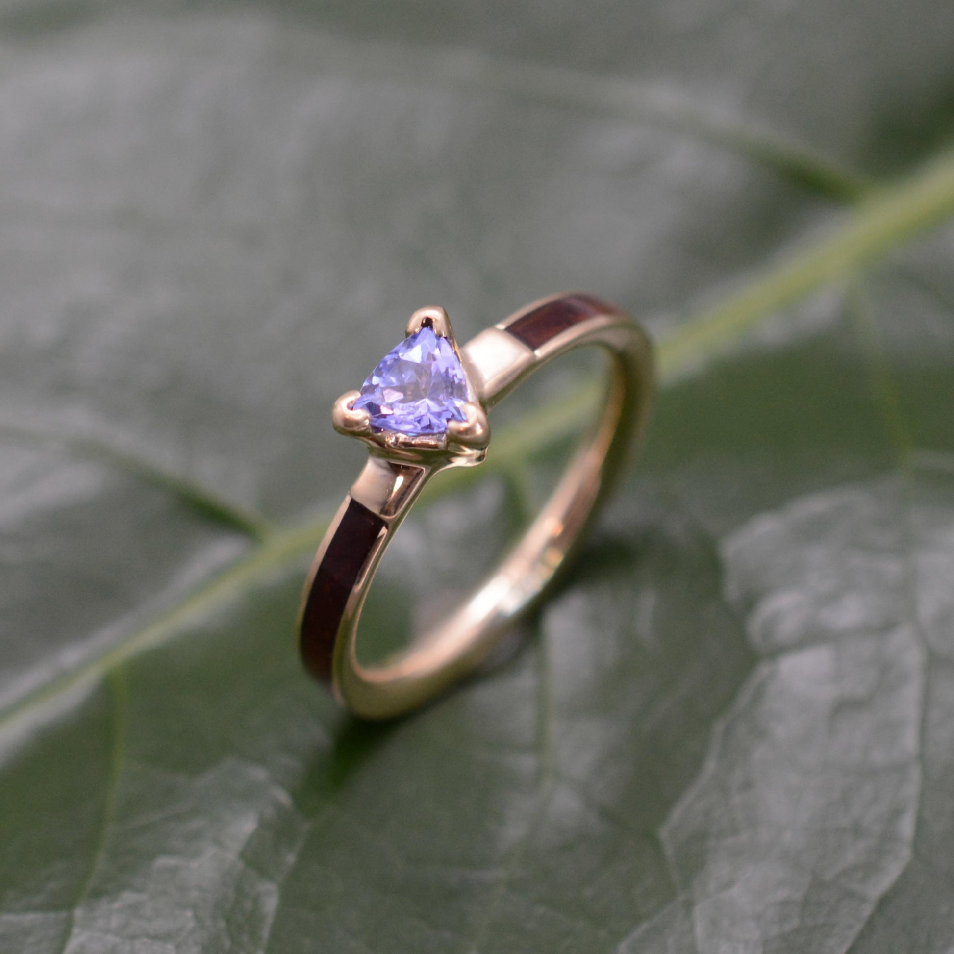 A gold ring with a purple gemstone, specifically a blue topaz, is displayed on a green leaf.
