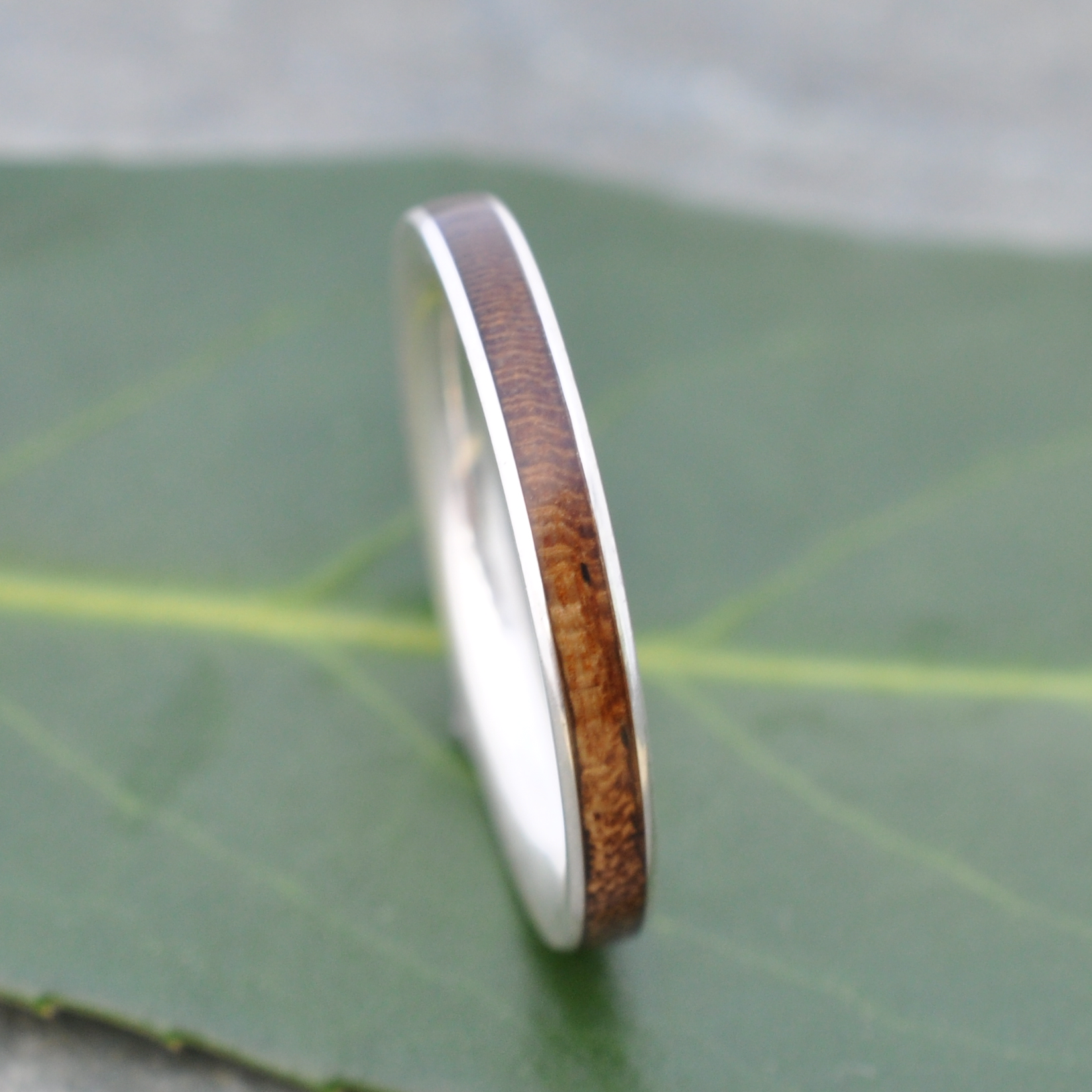A silver ring with a wooden band is resting on a green leaf.