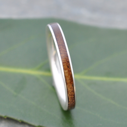 A silver ring with a wooden band is resting on a green leaf.