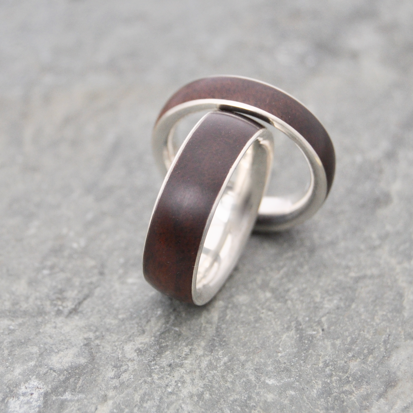 Two rings with dark wood and silver metal bands are placed on a gray surface.