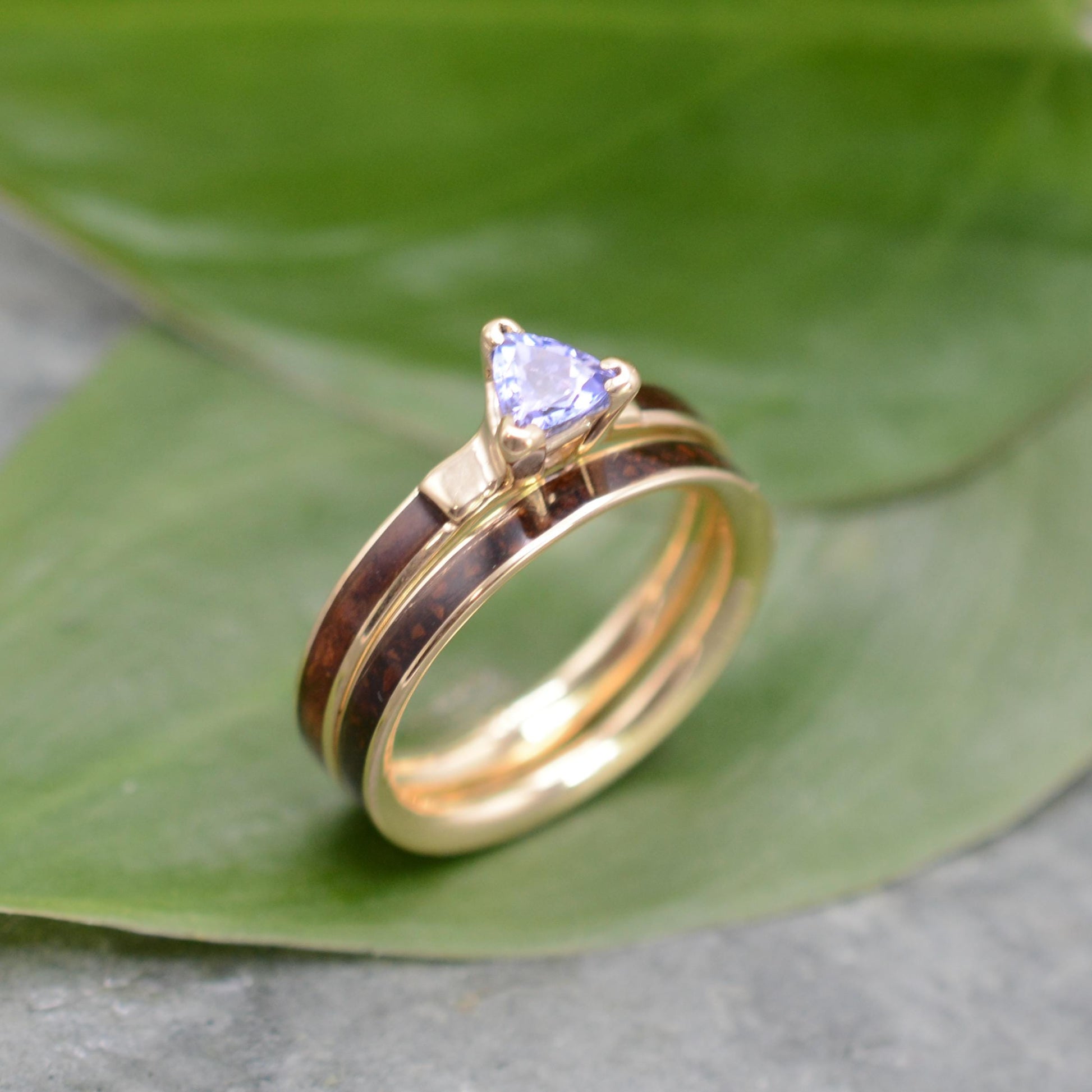 A gold ring with a blue gemstone, possibly a diamond, is displayed on a green leaf.