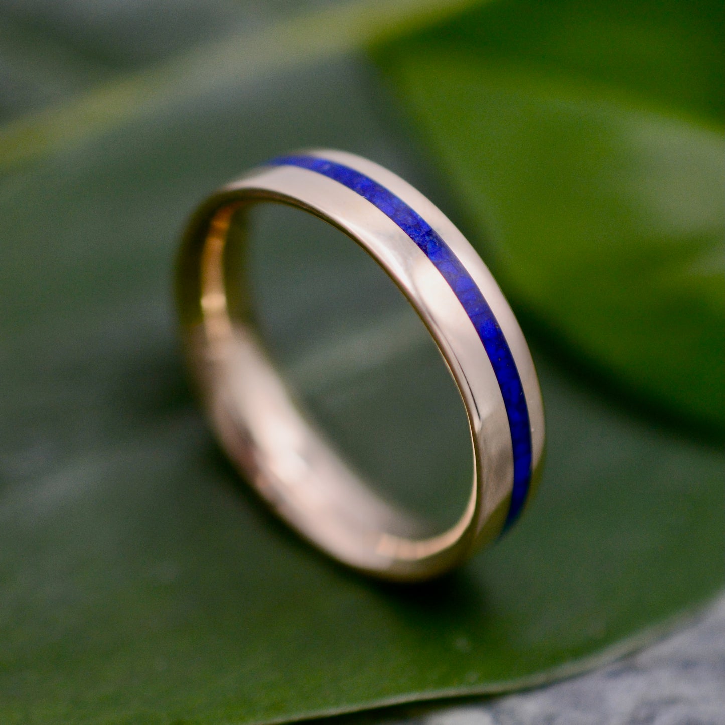 a gold ring with a blue stripe on top of a green leaf