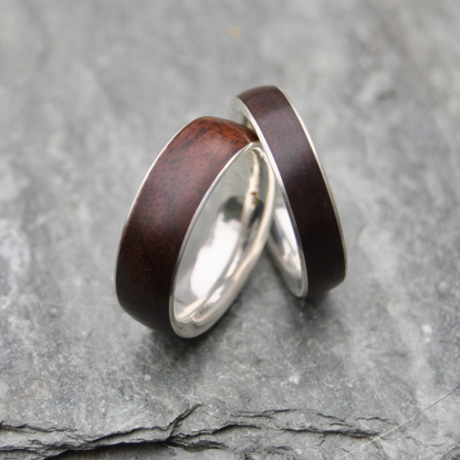 Two rings with dark wood and silver bands are placed on a gray rock surface.