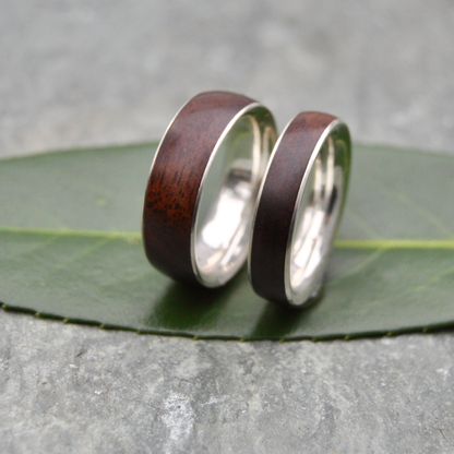 Two wooden wedding rings with silver bands resting on a green leaf.