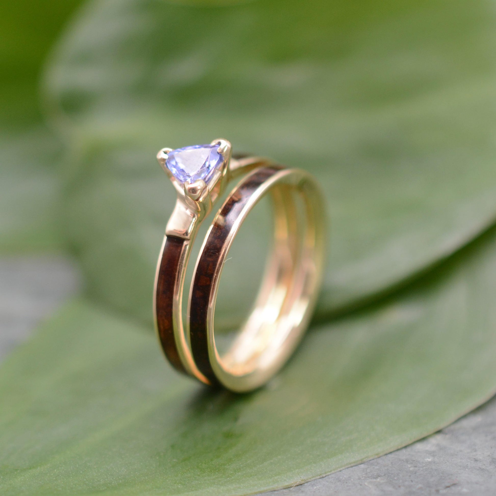 A gold ring with a purple gemstone is displayed on a green leaf.