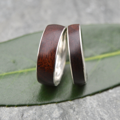 Two wooden wedding rings with silver bands resting on a green leaf.