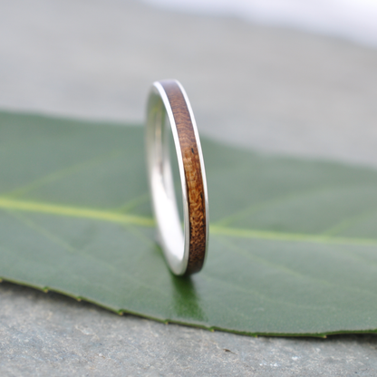 A silver ring with a wooden band is resting on a green leaf.