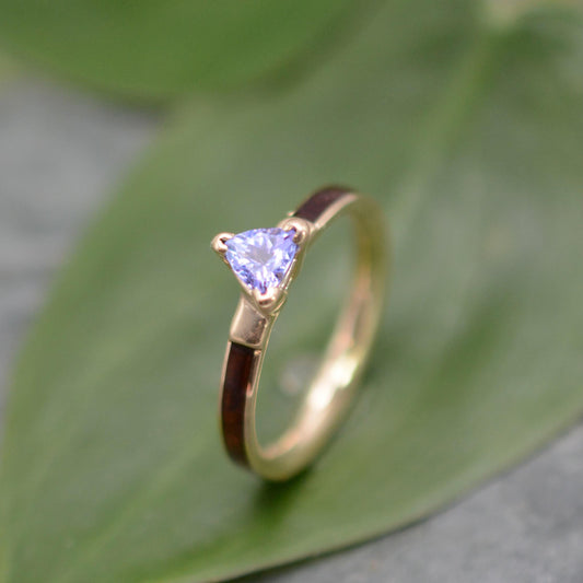 A gold ring with a purple gemstone, likely a sapphire, is displayed on a green leaf.