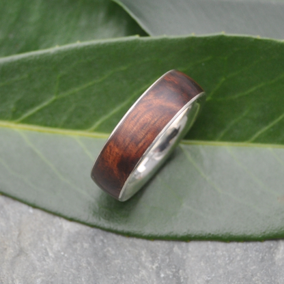 A wooden ring with a silver band is resting on a green leaf.