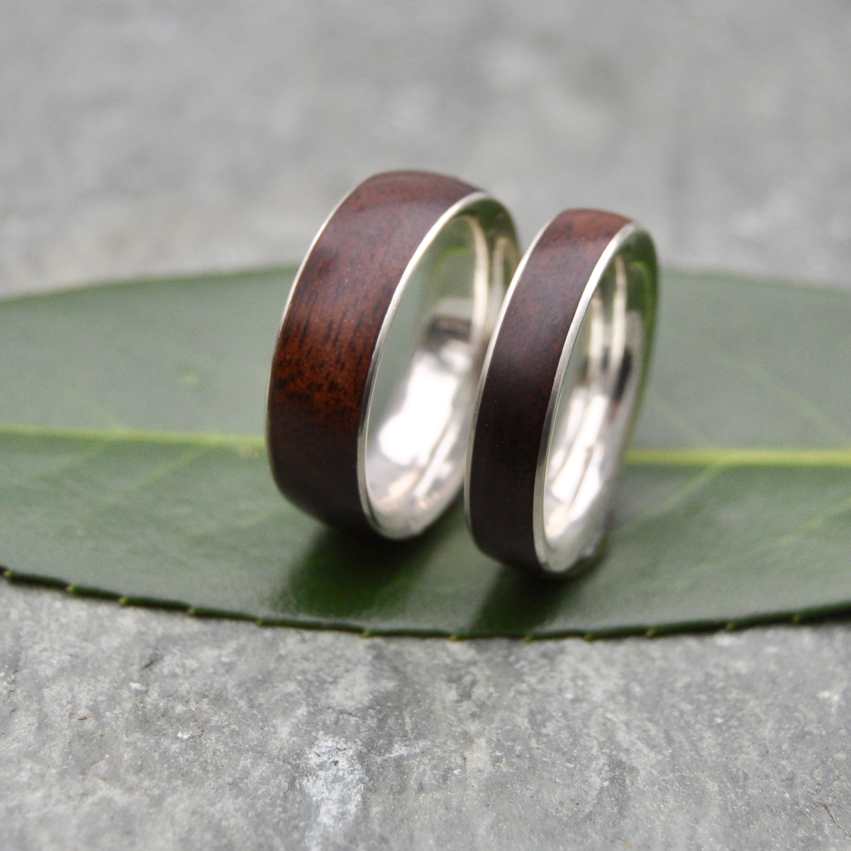 Two wooden wedding rings with silver bands resting on a green leaf.