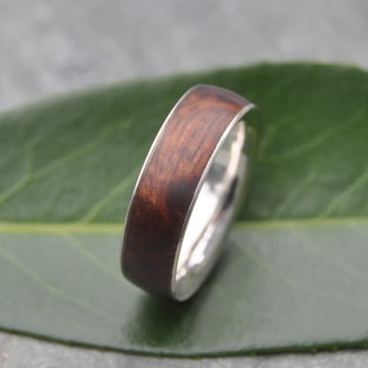 A wooden ring with a dark brown hue rests on a green leaf.