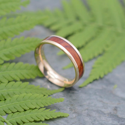 a gold ring with a wooden inlay sits on a fern leaf