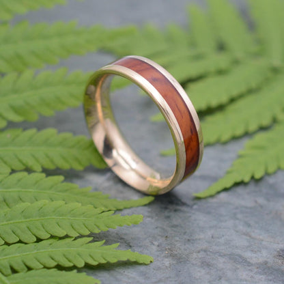 a gold ring with a wooden inlay sits on a fern leaf