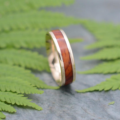 a wedding ring with a wooden inlay sits on a fern leaf