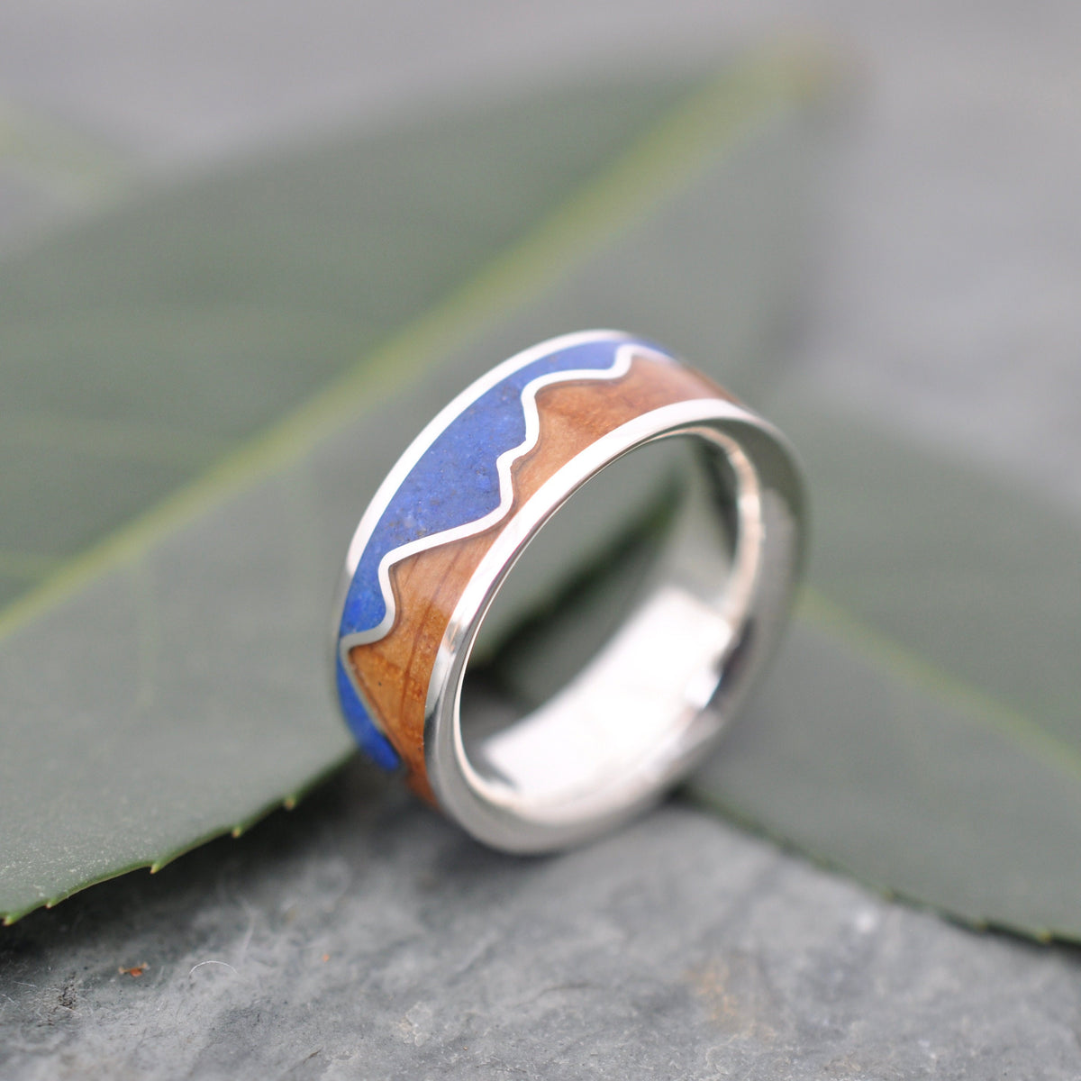 Lapis Lazuli Mountain Ring, Bourbon Barrel Wood and Sterling Silver on a leaf background, showcasing its unique design.