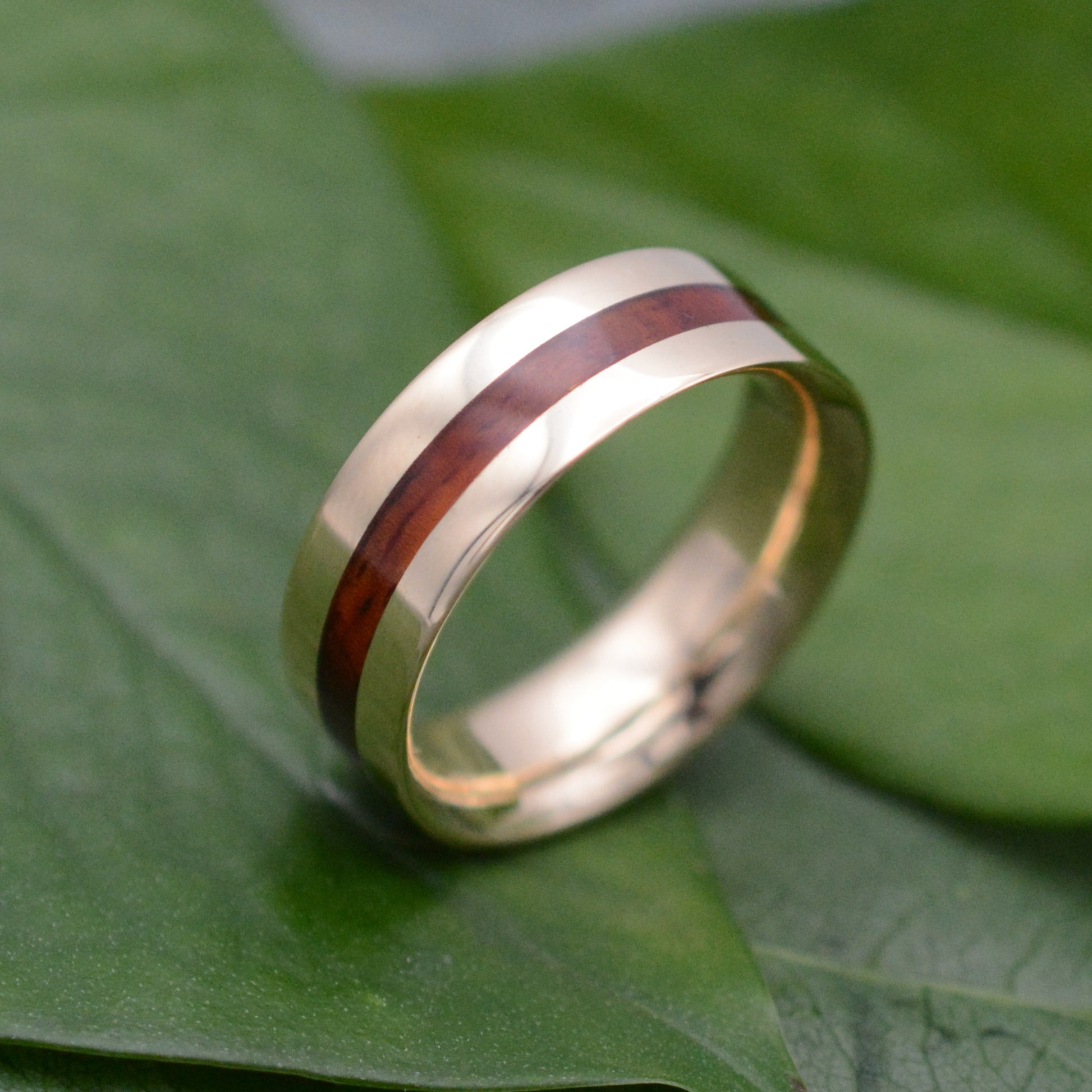 a gold ring with a wooden inlay on a green leaf