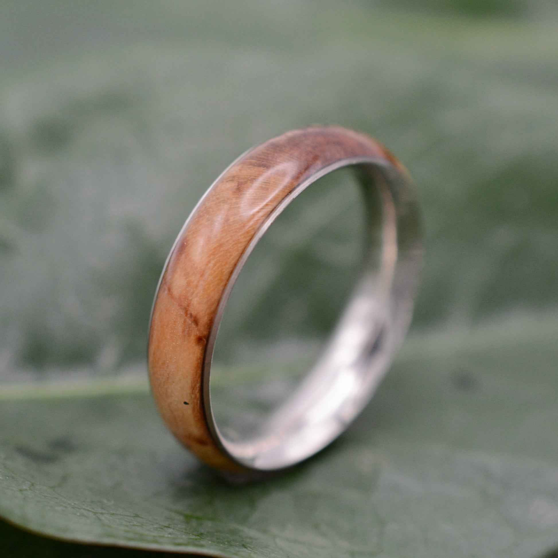 a wedding band with a wooden ring on top of a leaf