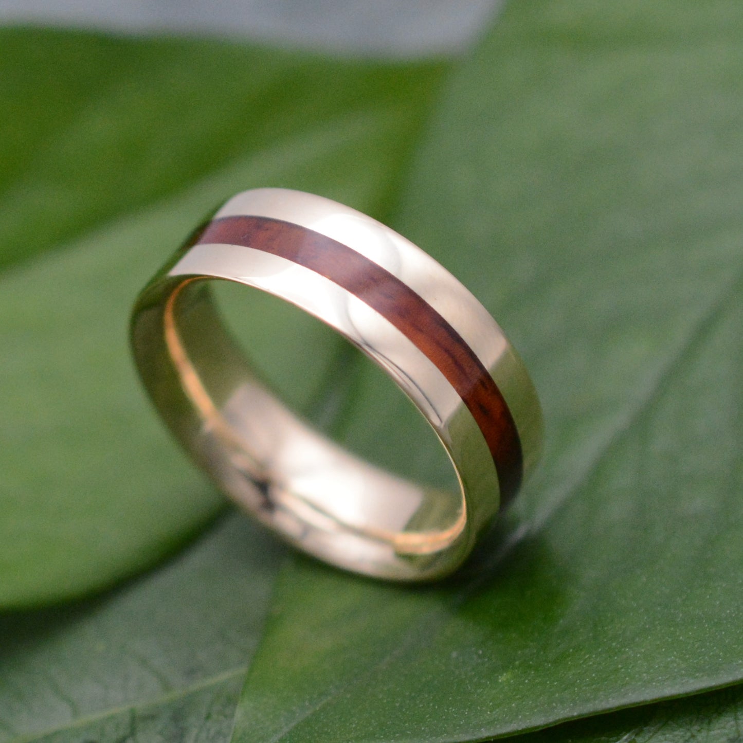 a gold ring with a wooden inlay on a green leaf
