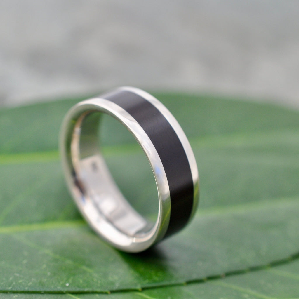 Lados Comfort Fit Lados Coyol Wood Sterling Silver Edges Wedding Ring on a green leaf, showcasing sleek design.