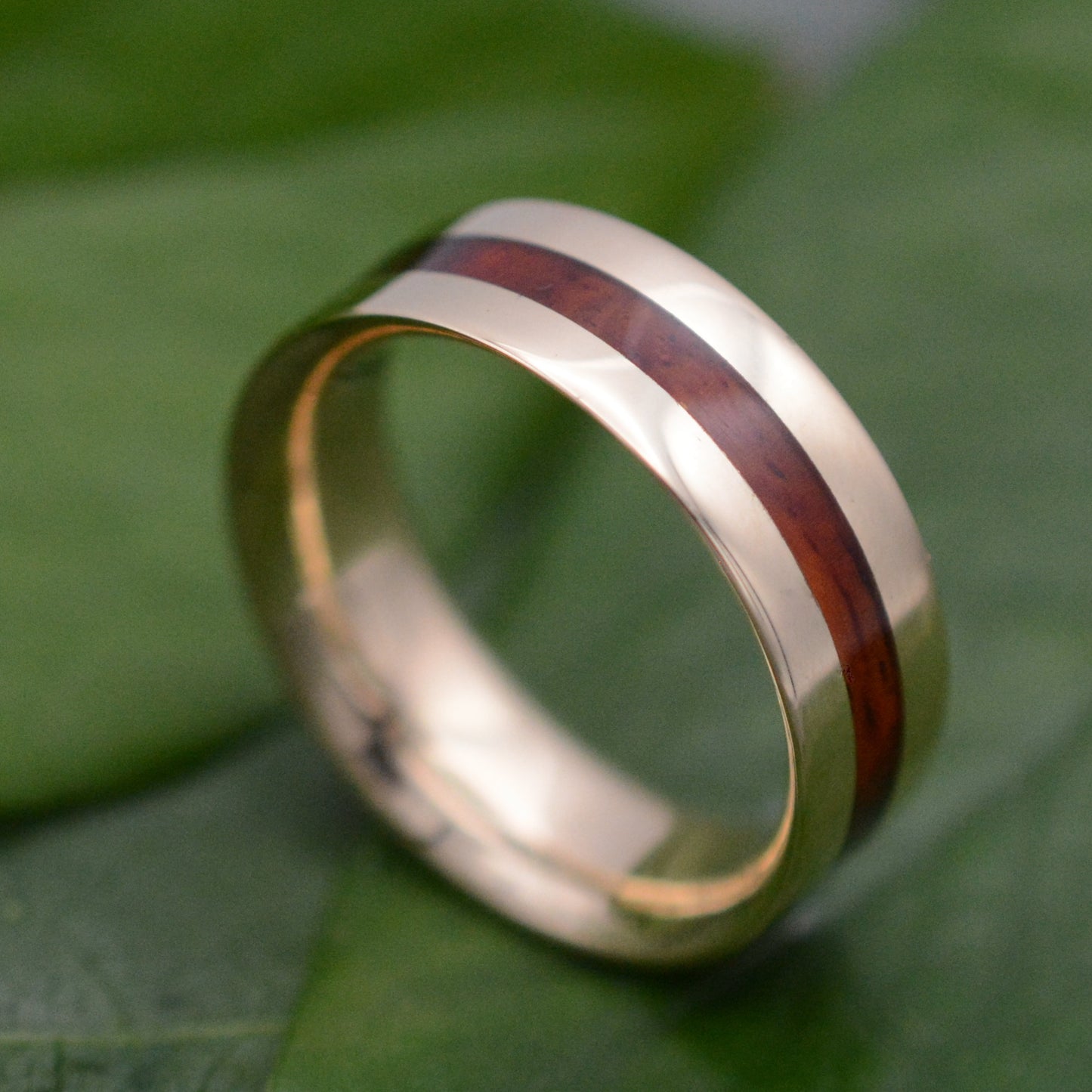a gold ring with a wooden inlay on a green leaf