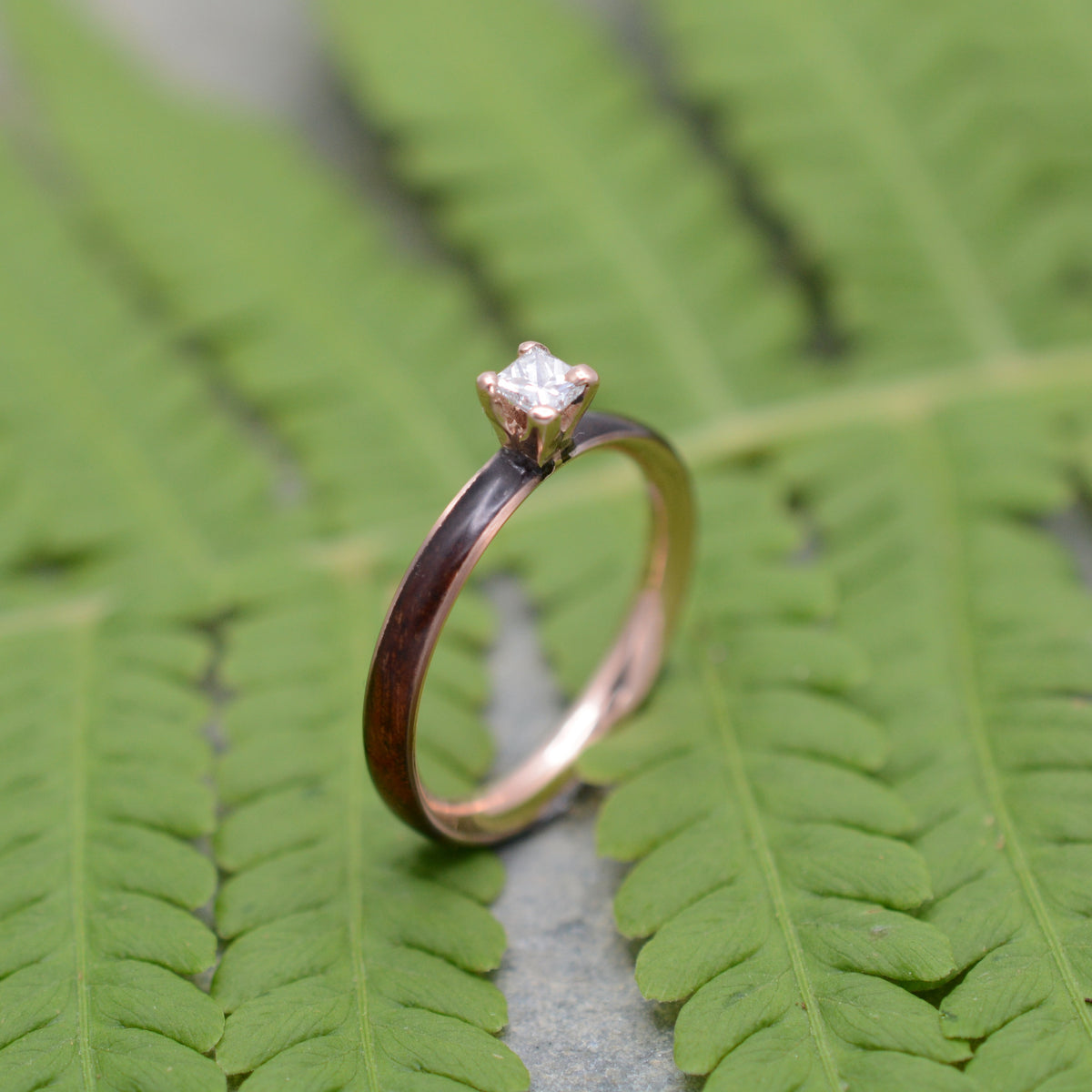 Rose gold diamond wood engagement ring with koa wood and princess cut diamond on natural background